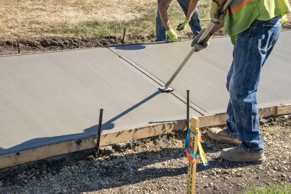 Workers pouring concrete in wooden mold for new sidewalk